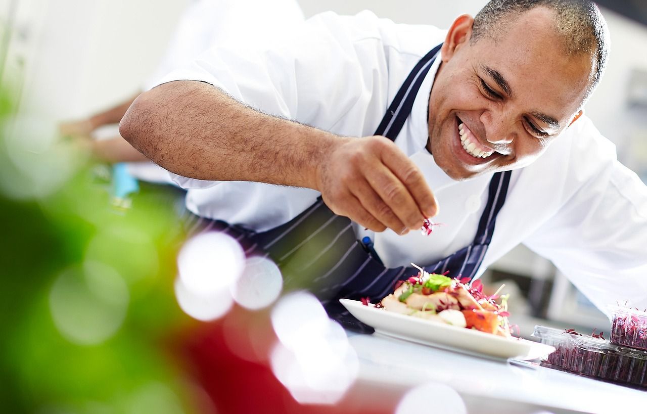 A chef meticulously garnishes a dish with fresh herbs, showcasing culinary precision and artistry in a professional kitchen setting. (Image via Pixabay)