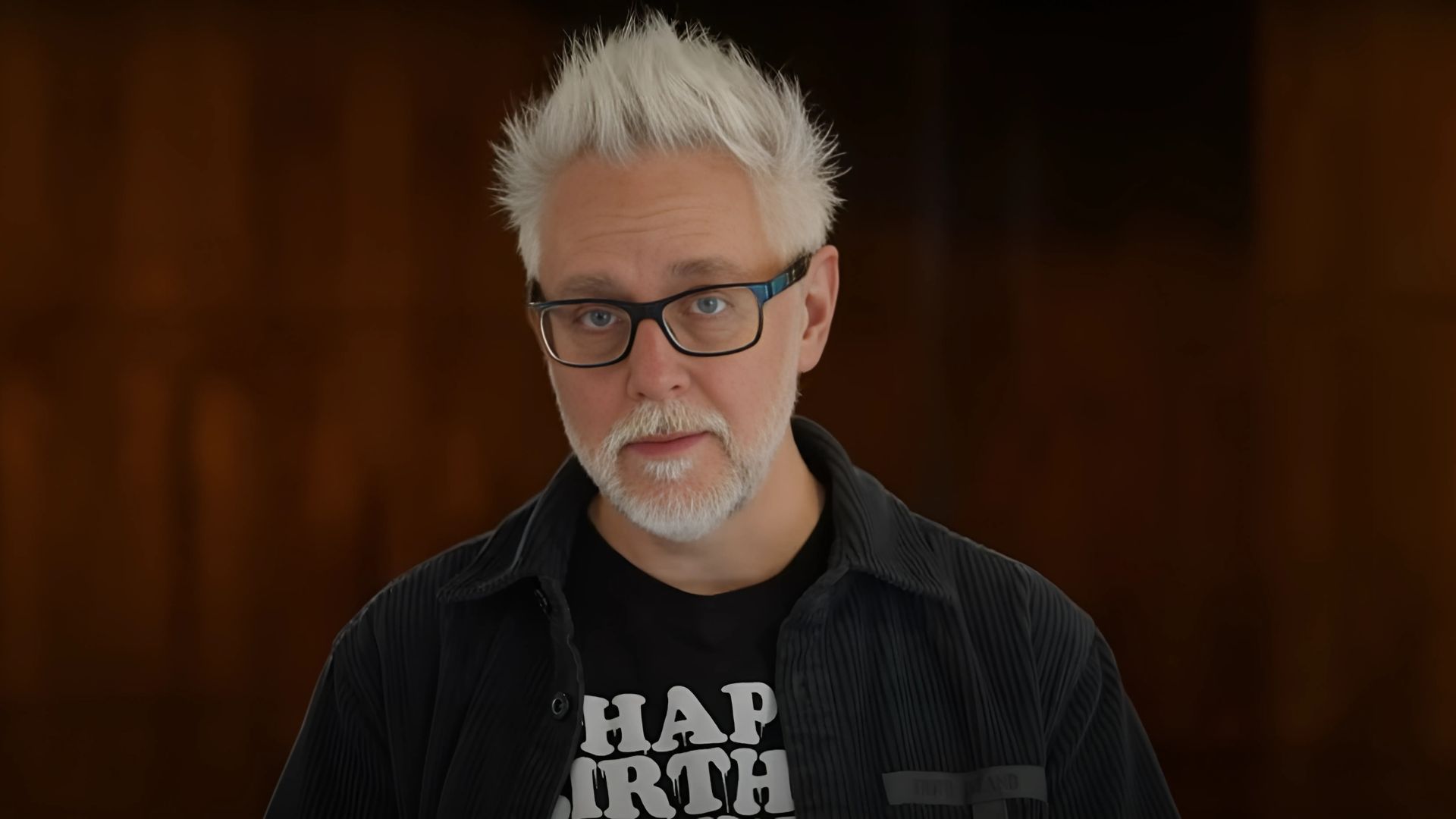 James Gunn is seen standing in front of a brown background