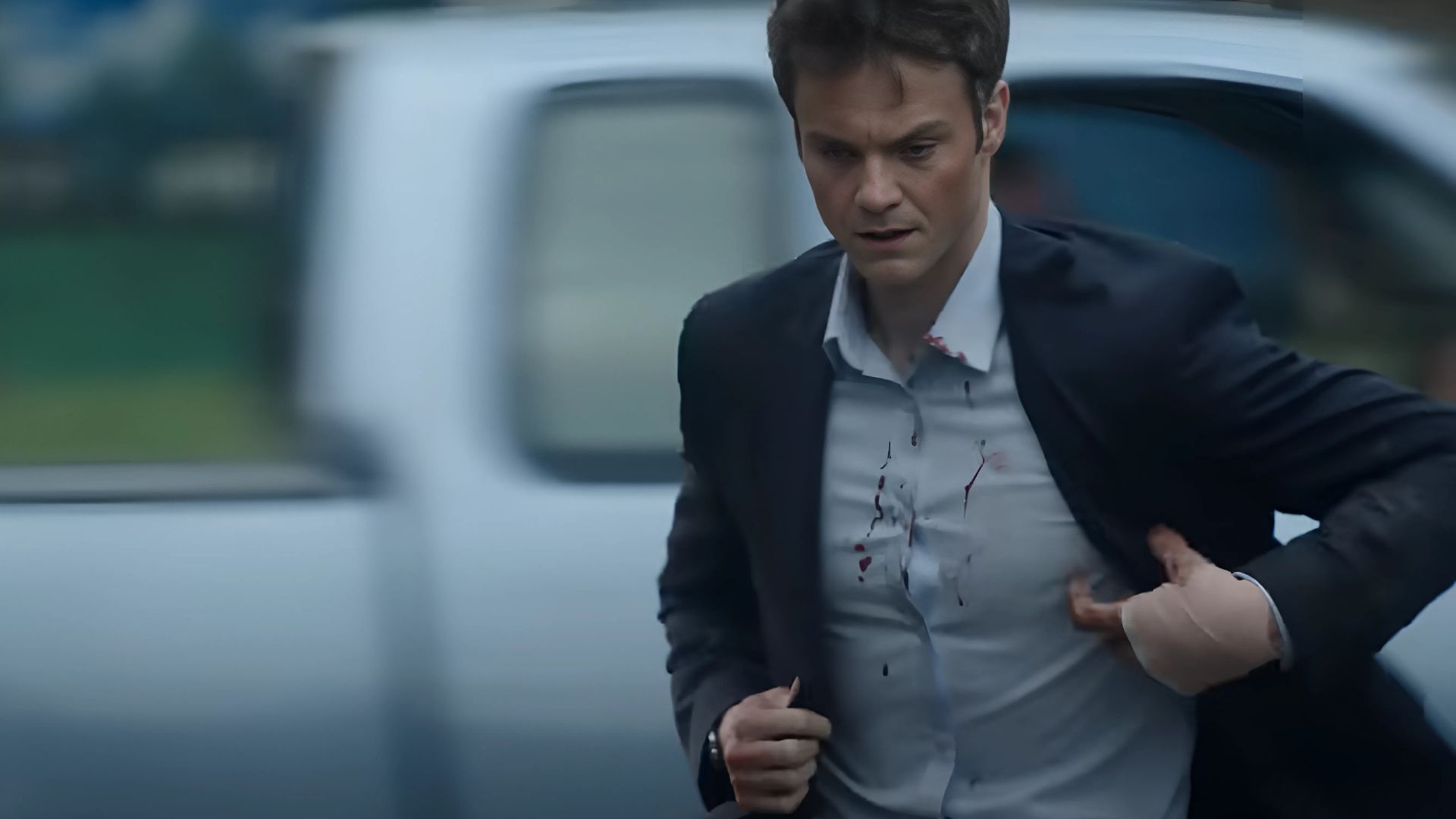 Jack Quaid adjusting his suit while walking down the road