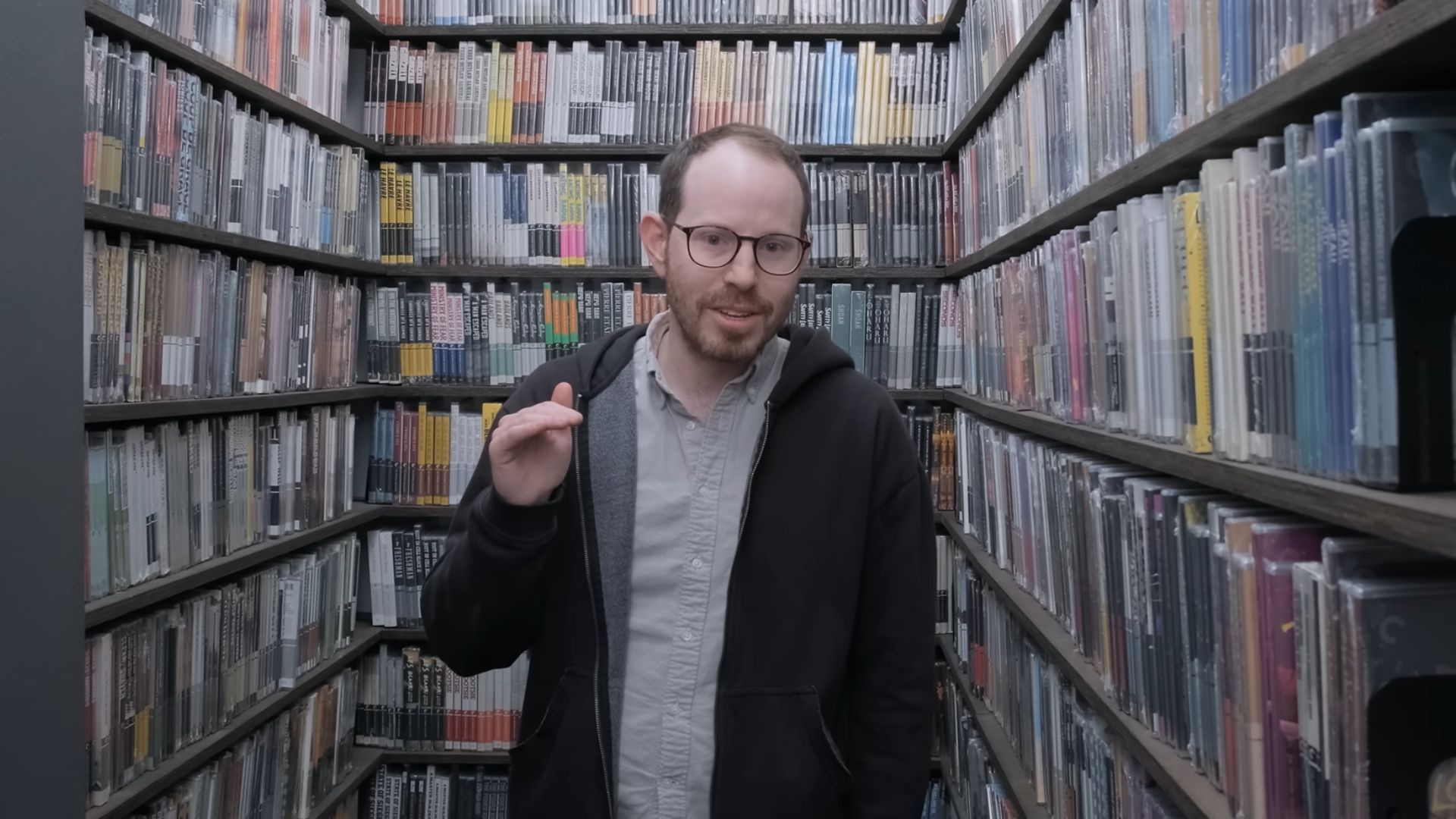 Ari Aster standing between book shelves