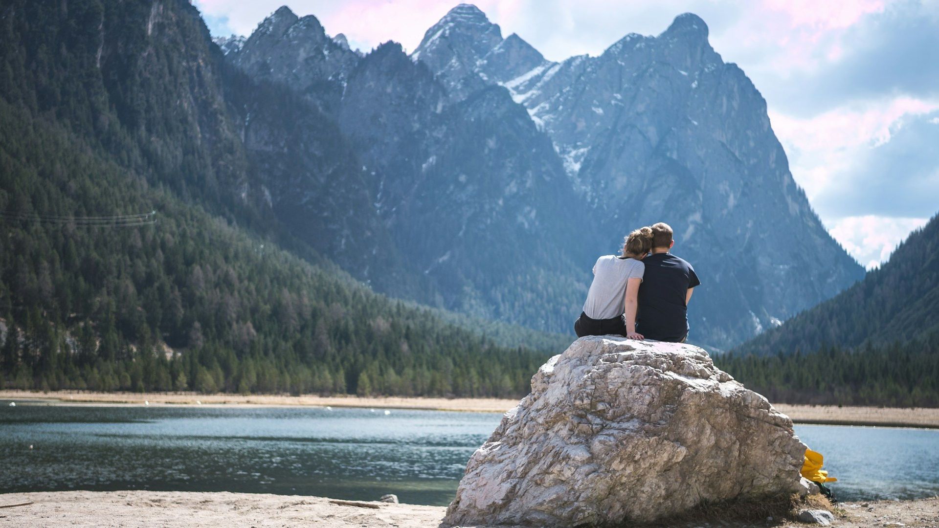 A couple sits on a rock looking oit over a lake: Source-Unsplash/ @Timo Stern)