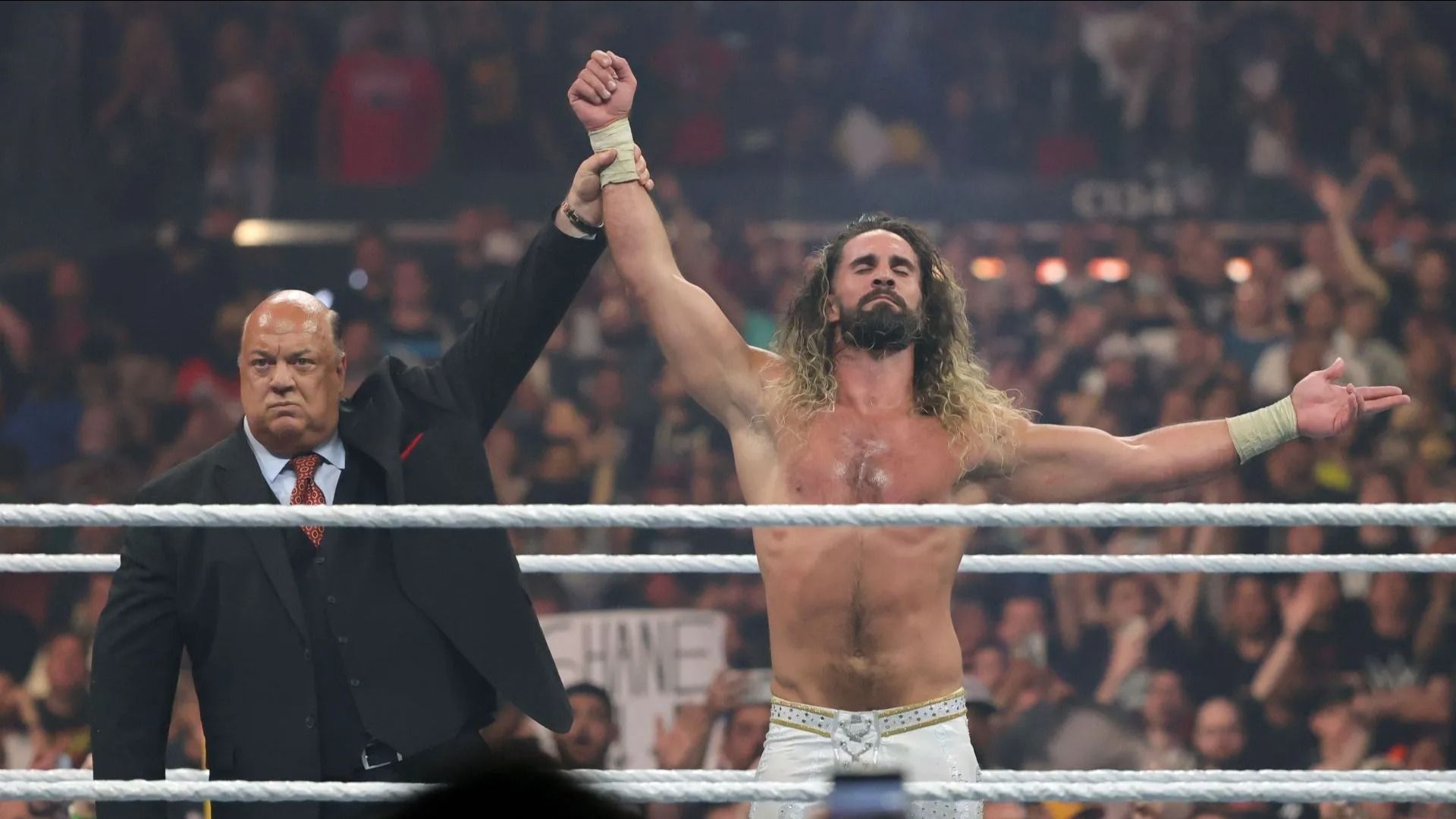 Paul Heyman (L) raises Seth Rollins
