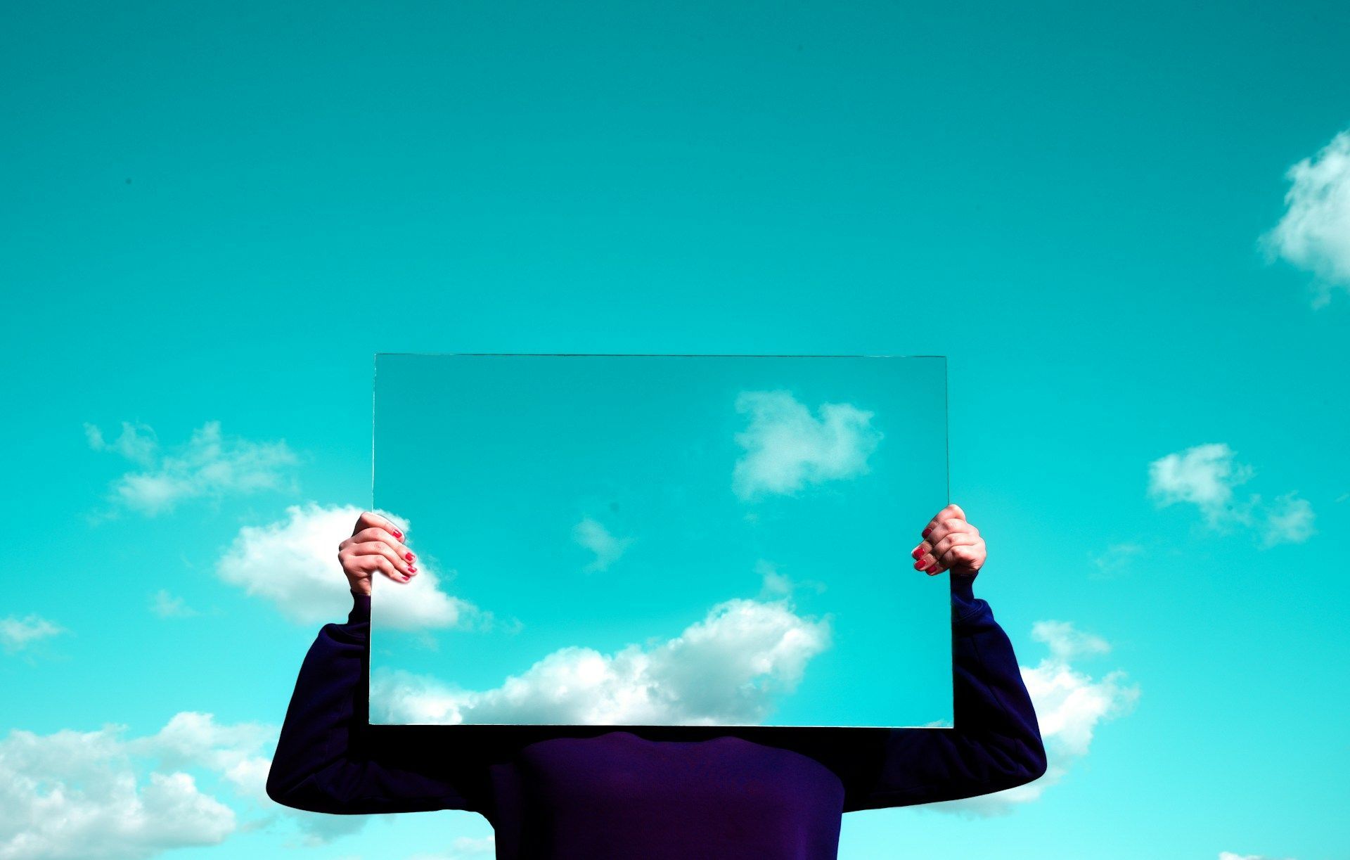 Image of boy holding a mirror reflecting sky (Image via Unsplash/Rishabh Dharmani)