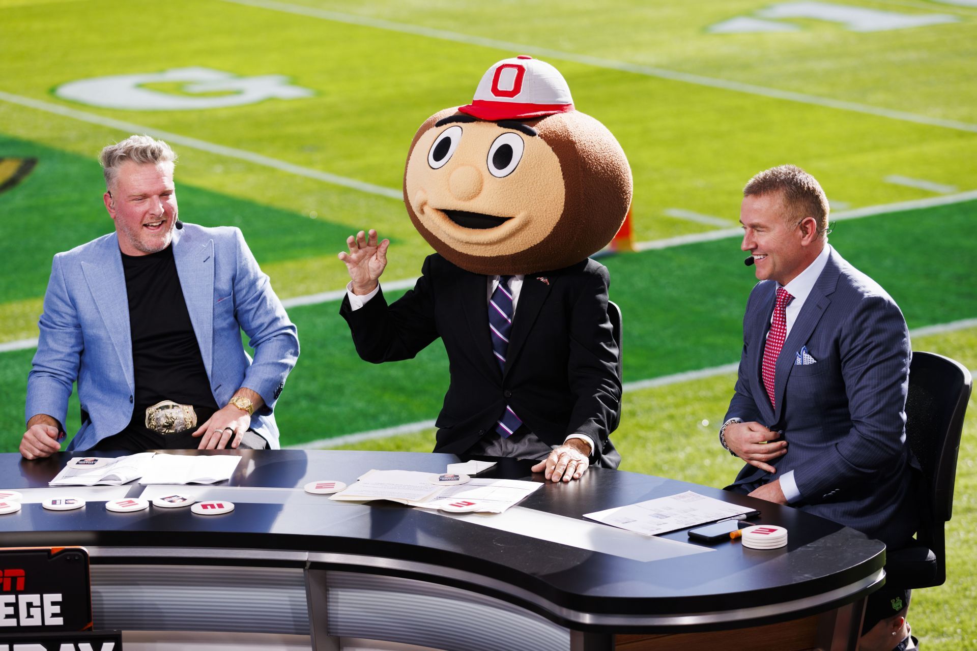 Corso [C] donning Brutus Buckeye headpiece, sitting with Pat McAfee [L] and Kirk Herbstreit [R] during a Ohio State vs Oregon (Image via Getty/Ric Tapia)