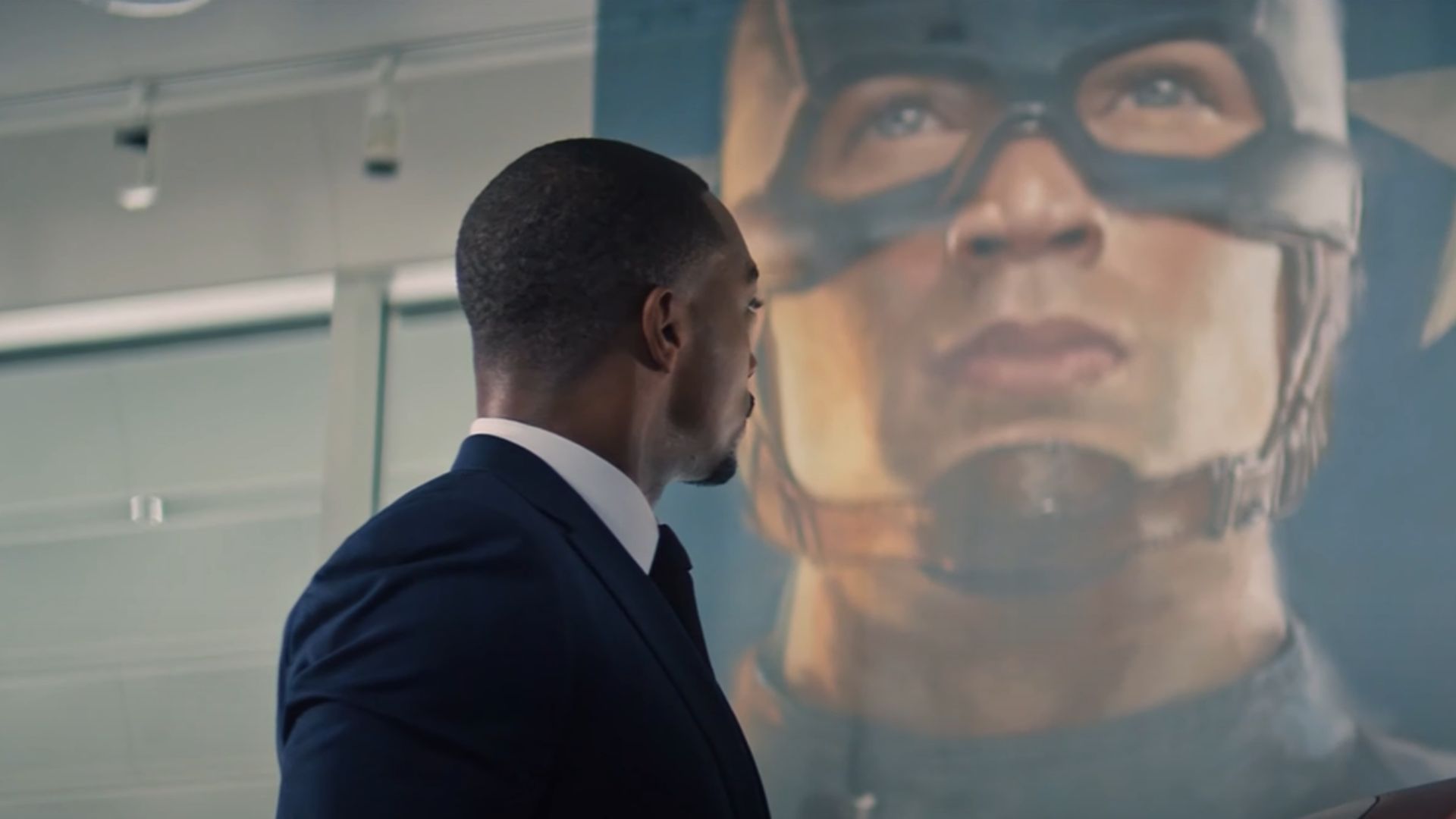 Anthony Mackie looks at a picture of Captain America while holding the shield